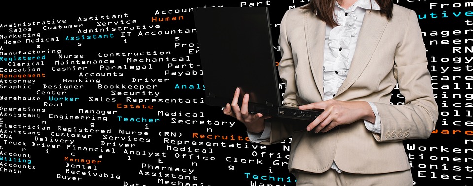 A faceless business woman, holding a laptop, standing in front of a wall of misc. code.